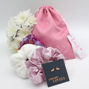 Pink drawstring bag with flowers, scrunchies, and earrings on a light gray background