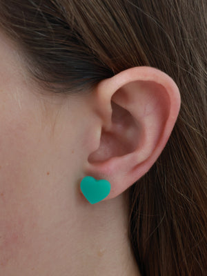Grateful teal acrylic heart stud earrings worn on an ear to show size and fit