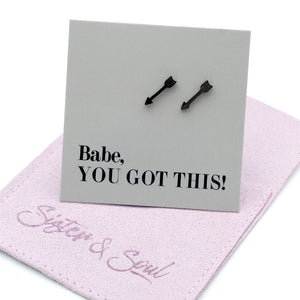 Black arrow-shaped stud earrings displayed on a gray card that reads 'Babe, YOU GOT THIS!' with a Purple branded jewelry pouch underneath.