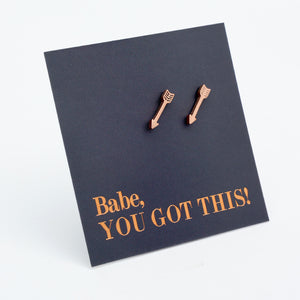 Rose gold arrow stud earrings on a dark navy blue display card that reads 'Babe, YOU GOT THIS!' in rose gold lettering, set against a clean white background.