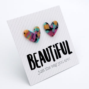 A pair of marbled heart-shaped stud earrings in a multicolor mix of pink, yellow, blue, and black, displayed on a white card with the text 'BEAUTIFUL just the way you are!'.