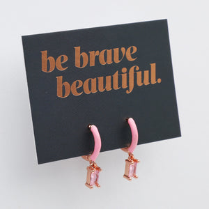 Pink earrings on a card with 'be brave beautiful' text on a white background
