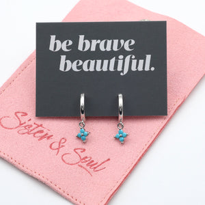 Silver earrings with blue accents on a 'be brave beautiful' card with pink background