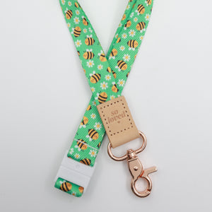 So Loved embossed on a green bee and daisy lanyard with tan trim and a lobster clasp.