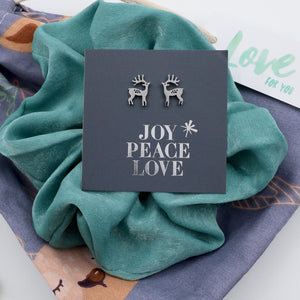 Deer earrings on a card with 'Joy Peace Love' text, placed on a teal fabric background.