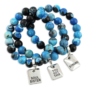 Blue and black beaded bracelets with motivational charms on a white background