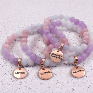 Set of beaded bracelets with rose gold charms on a textured surface