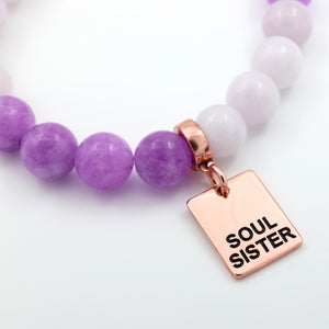 Bracelet with purple and white beads and a rose gold 'Soul Sister' charm on a light background