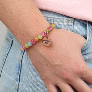 Multicolored beaded bracelet with a 'Choose Joy' charm on a wrist, against a light background.