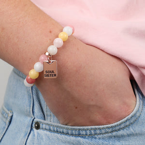 Pink and yellow stone bead bracelet with soul sister charm, and person with hand in a pocket.