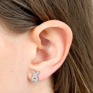 Close-up of an ear wearing a small silver bunny-shaped earring.