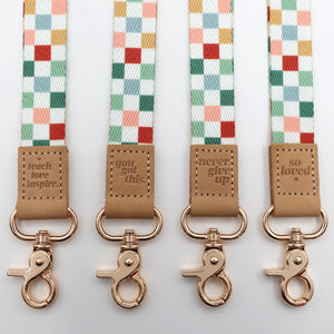 Four checkered lanyards with brown leather tags and rose gold clasps on a light gray background.