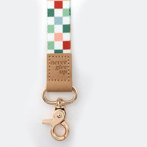 Checkered ribbon with a brown leather tag and rose gold clasp on a white background
