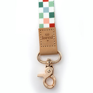 Checkered ribbon with 'so loved' leather patch and gold clasp on a white background