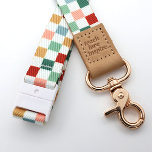 Colorful checkered strap with a rose gold clasp and 'teach love inspire' tag on a white background