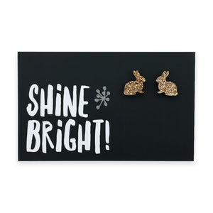 A pair of champagne gold acrylic bunny stud earrings displayed on a black card with the text 'SHINE BRIGHT!' and a star symbol.