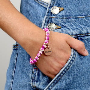 Pink speckled stone bracelet on womans wrist wearing denim overalls.