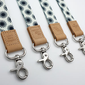 Three lanyards with floral pattern and leather tags on a light gray background
