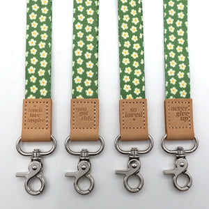 Four green floral patterned straps with brown leather accents and metal clasps on a white background.