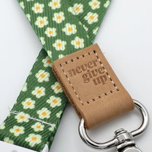 Green floral-patterned strap with a brown leather tag and silver keychain on a white background