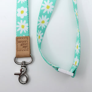 Lanyard with daisy pattern and 'never give up' leather tag on a light gray background