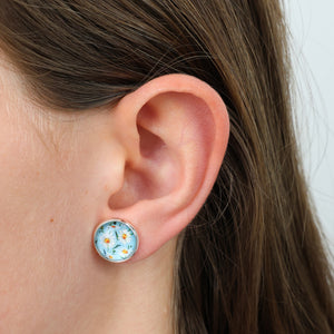 Close-up of an ear wearing a floral stud earring with a light blue background.