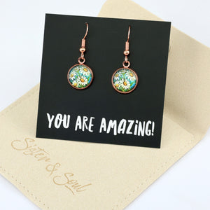 Daisy-themed earrings on a 'You Are Amazing!' card with a beige pouch underneath.