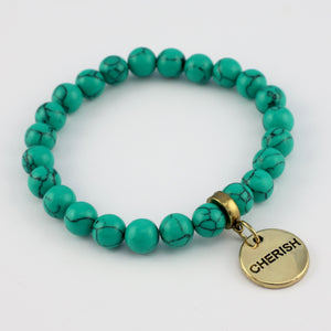 Turquoise beaded bracelet with a gold charm on a white background