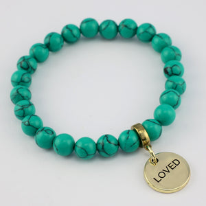 Turquoise beaded bracelet with a gold 'LOVED' charm on a white background