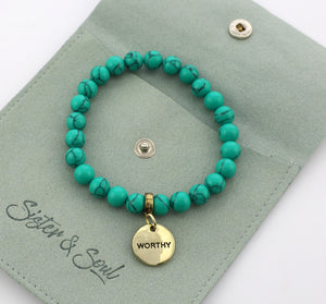 Turquoise beaded bracelet with a gold 'WORTHY' charm on a green card with 'Sister & Soul' branding.