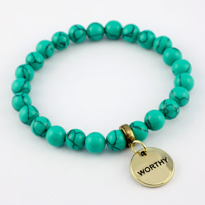 Turquoise beaded bracelet with a gold 'WORTHY' charm on a white background