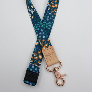 So Loved embossed on a dark blue floral lanyard with tan trim and a lobster clasp.