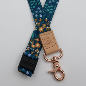 Teach Love Inspire embossed on a dark blue floral lanyard with tan trim and a lobster clasp.