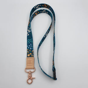 Teach Love Inspire embossed on a dark blue floral lanyard with tan trim and a lobster clasp.