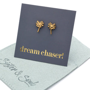 Gold dandelion-shaped earrings on a card with 'dream chaser!' text, displayed on a light blue mat.