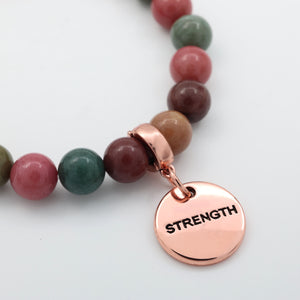 Bracelet with multicolored beads and a rose gold 'STRENGTH' charm on a light background