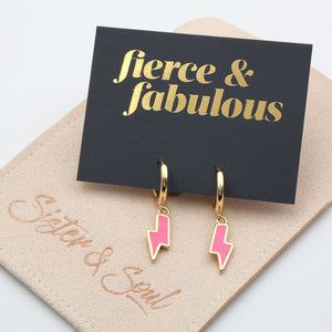 Pink lightning bolt shaped huggies dangle earrings presented on a grey card with gold 'Fierce & Fabulous' writing on a oat 'Sister & Soul' pouch.