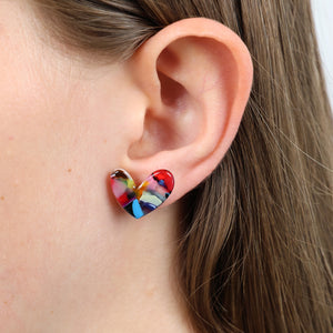 A close-up of a person's ear wearing a small heart-shaped earring with a multicolor marbled pattern in red, blue, yellow, and white.