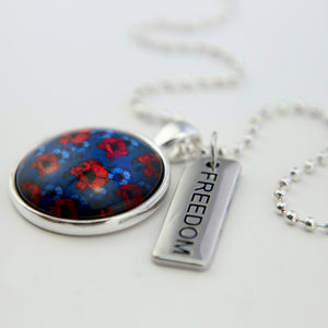 Poppies print pendant necklace in silver with freedom word charm and white background.