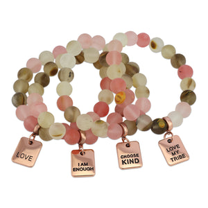 A collection of stone bracelets with rose gold charms, featuring beads in pink and earthy tones, with charms that say 'LOVE', 'I AM ENOUGH', 'CHOOSE KIND', and 'LOVE MY TRIBE'.
