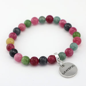 Multicolored beaded bracelet with a 'GRATEFUL' charm on a white background