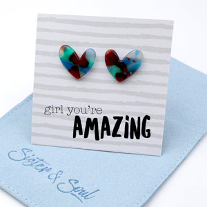 Heart-shaped stud earrings with a marbled red, blue, and green pattern, displayed on a white card that reads 'girl you're AMAZING' with a light blue fabric pouch underneath.