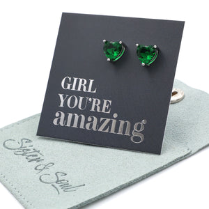 Green heart-shaped earrings on a card with 'Girl you're amazing' text, displayed on a green surface.