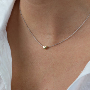 Necklace with a heart-shaped pendant on a person wearing a white shirt.