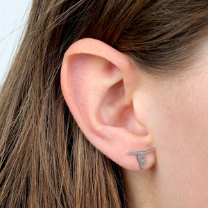 Close-up of an ear wearing a silver gymnastics shaped earring with a small design.