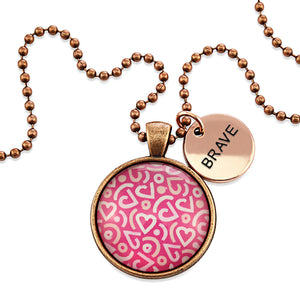 Pink heart print vintage red copper circle pendant necklace with 'brave' charm. A fundraising product for the national breast cancer foundation.