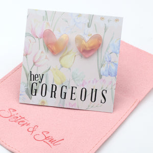 Heart-shaped earrings on a card with 'hey gorgeous' text on a pink pouch