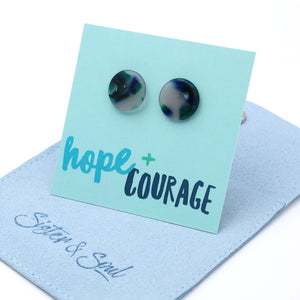 Round stud earrings with a marbled pattern of navy, green, and white, displayed on a light blue card that reads 'hope + COURAGE'. The card is propped up on a light blue velvet jewelry pouch embroidered with 'Sister & Soul'.