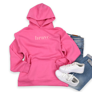Pink hoodie with 'brave' text, white sneakers, and blue jeans on a white background