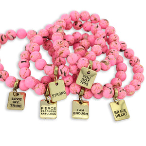 Pink beaded bracelet with gold charm tags on a white background